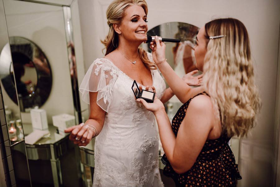 Charlie applying bridal makeup to a smiling bride in her wedding dress